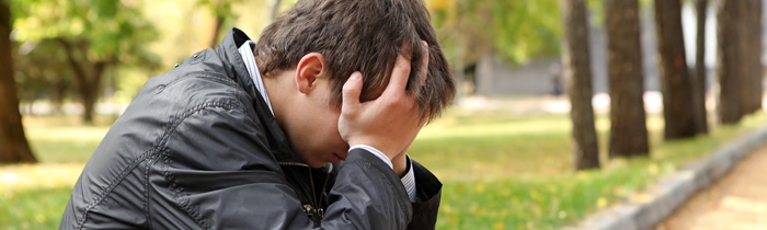 Mand sidder med ansigtet i hænderne i en park